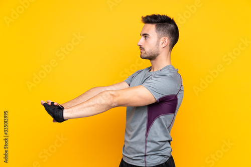 Sport man over isolated yellow wall stretching arm © luismolinero