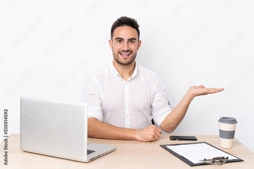 Young business man with a mobile phone in a workplace extending hands to the side for inviting to come Young business man with a mobile phone in a workplace extending hands to the side for inviting to come