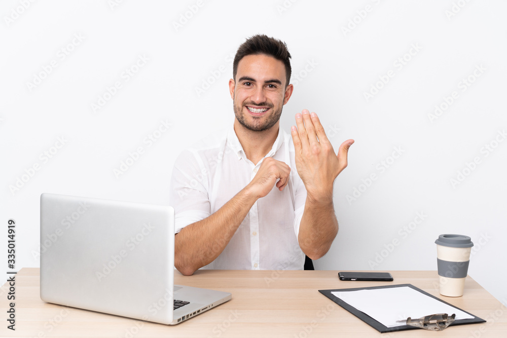 Young business man with a mobile phone in a workplace inviting to come Young business man with a mobile phone in a workplace inviting to come