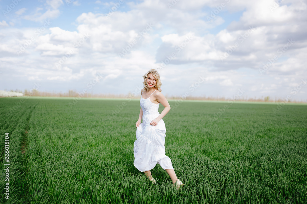 blonde girl in a white dress sits on the green fresh spring grass, blue sky blonde girl in a white dress sits on the green fresh spring grass, blue sky