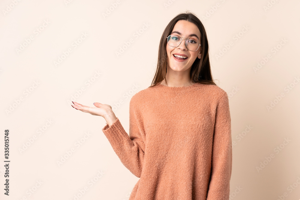 Young woman over isolated beige background holding copyspace imaginary on the palm to insert an ad Young woman over isolated beige background holding copyspace imaginary on the palm to insert an ad