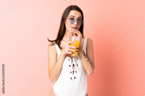 Young woman over isolated pink background in swimsuit and holding a cocktail