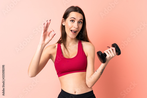 Young sport woman making weightlifting over isolated pink background showing ok sign with fingers