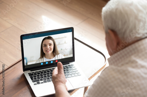 Back view of mature father have pleasant online conversation on laptop with happy millennial daughter, senior man talk speak on video call with female consultant, use webcam on modern computer