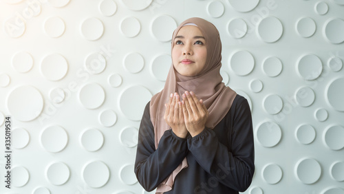 Pretty young female Muslim in tradidtional clothes praying with muslem hands while standing and meditation with circle pattern background. photo