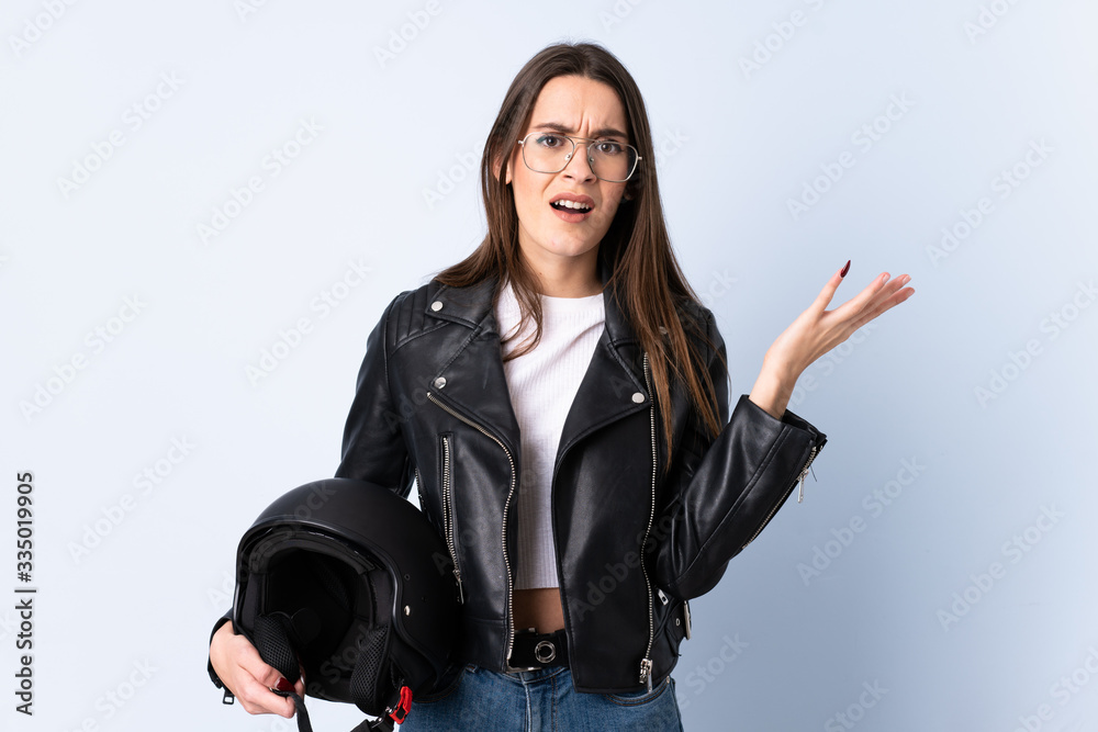 Young woman holding a motorcycle helmet over isolated blue background unhappy and frustrated with something Young woman holding a motorcycle helmet over isolated blue background unhappy and frustrated with something