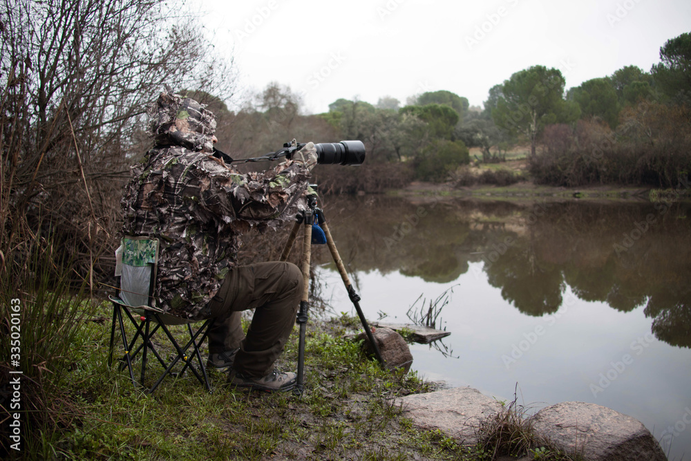 Wildlife photographer sitting and camouflaged on the bank of a river stalking wild animals.