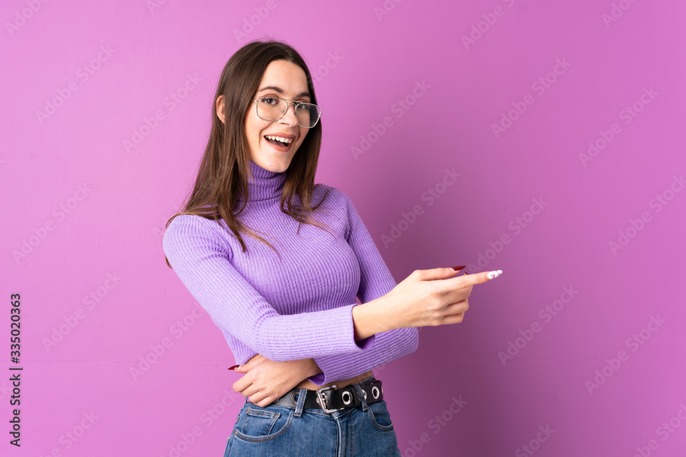 Young woman over isolated purple background pointing finger to the side and presenting a product Young woman over isolated purple background pointing finger to the side and presenting a product