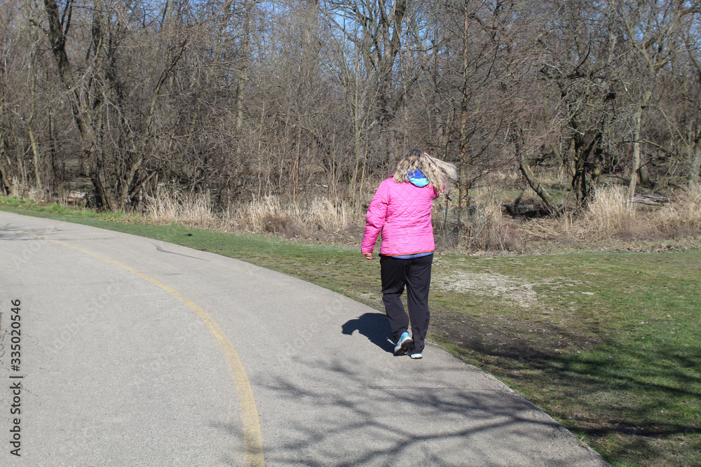 Fototapeta premium Woman with blonde hair blowing in the wind in a pink coat walking on the North Branch Trail at Chicago's Bunker Hill Woods