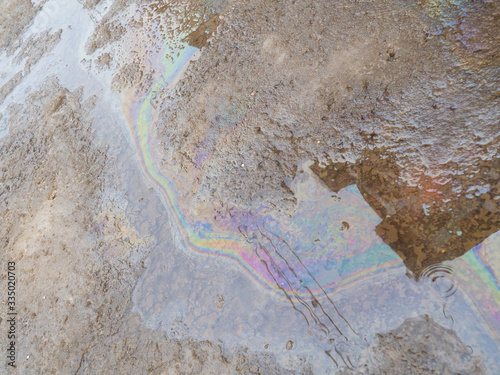 Spill of petrol in the road puddle. Gasoline footprint rainbow on the asphalt. Concept of ecological problem of environmental pollution. Multicolored streaks, reflection of houses and wires