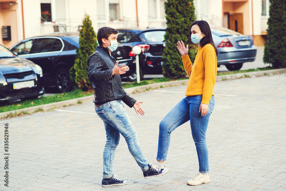 Young couple greeting with foots. Girl and guy wearing face masks outdoors. Coronavirus epidemic.