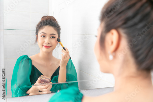 Young beautiful woman happy and making make-up near mirror in room.
