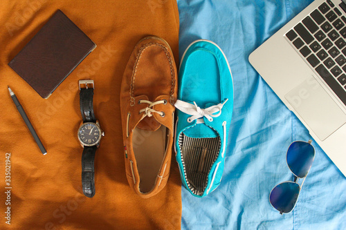 Two casual shoes of different colors bordered with colors and surrounded by laptop keyboard, mobile phone, watches, glasses, pen and notebook. Brown and blue version. Top view. Flat lay. (ID: 335021942)