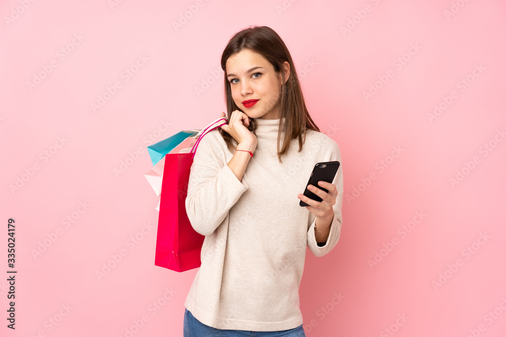 Teenager girl isolated on pink background holding shopping bags and a mobile phone Teenager girl isolated on pink background holding shopping bags and a mobile phone