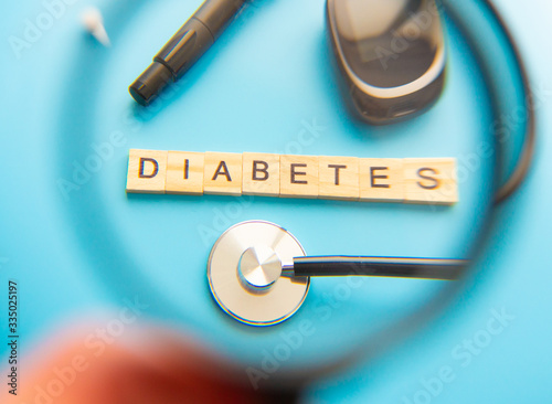 Diabetes Wooden Text. Medicine, Diabetes, Glycemia, Health care and people concept - close up of lancelet, Glucose meter and stethoscope on blue background. photo