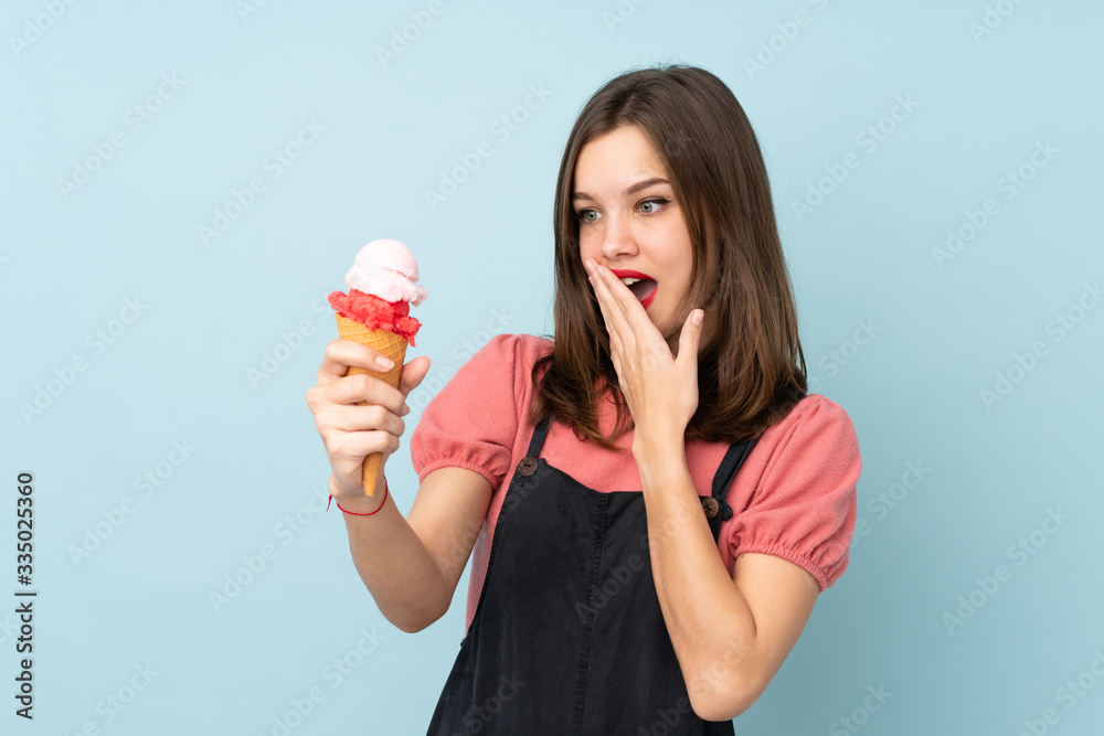 Teenager girl holding a cornet ice cream isolated on blue background with surprise and shocked facial expression Teenager girl holding a cornet ice cream isolated on blue background with surprise and shocked facial expression