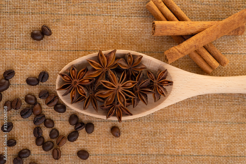 Wooden spoon with star anise on the table on a napkin, next to coffee beans and cinnamon sticks close-up. Wooden spoon with star anise on the table on a napkin, next to coffee beans and cinnamon sticks close-up.