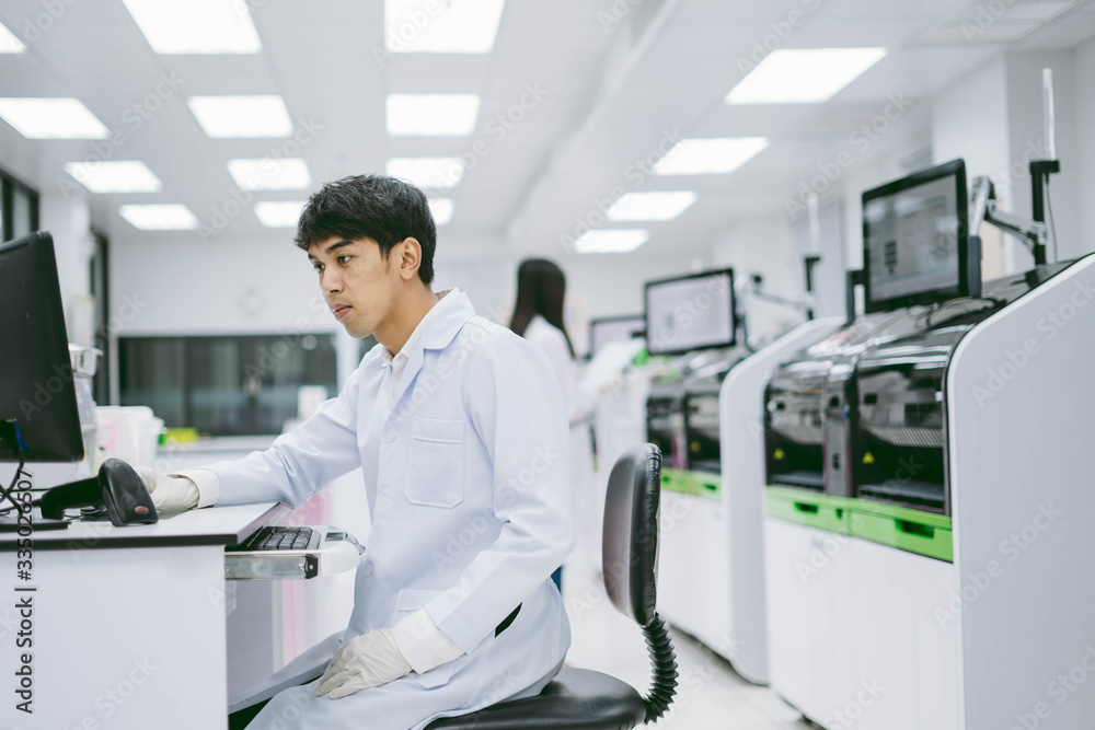 young male scientist looking results from automation blood analyzer report in computer and young female scientist working with automation blood analyzer at medical laboratory