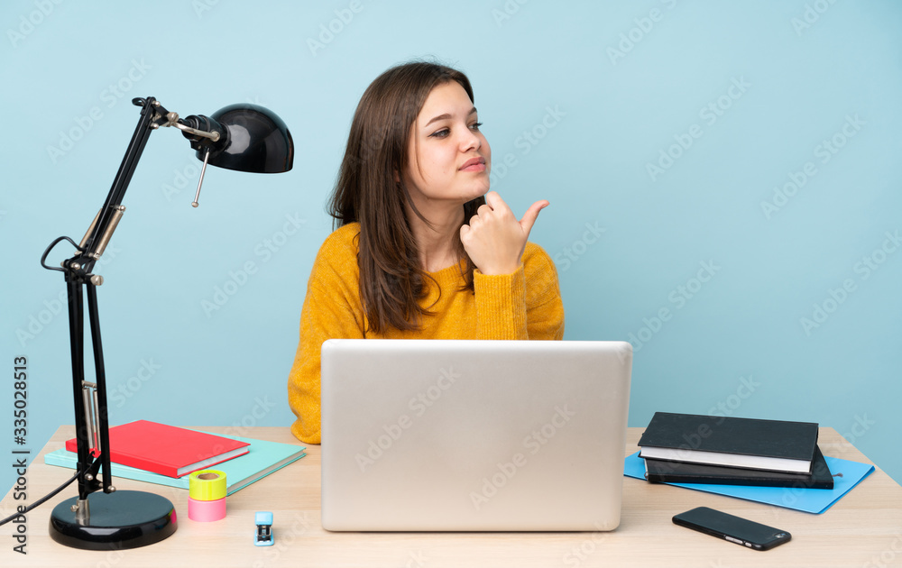 Student girl studying in her house isolated on blue background pointing to the side to present a product Student girl studying in her house isolated on blue background pointing to the side to present a product