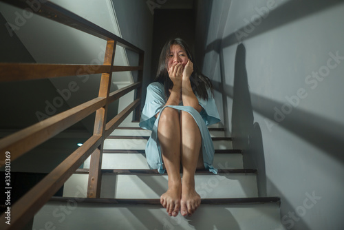 Asian horror movie style portrait of young adult sad and desperate Chinese woman or teenager girl suffering depression problem or mental disorder sitting on staircase at home