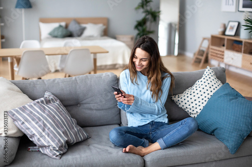 Smiling young woman at home using modern smartphone. Online chat.