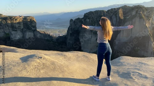 Young woman hiker with arms wide open at the top of the mountain watching a beautiful scenery at sunset