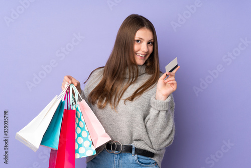 Teenager caucasian girl isolated on purple background holding shopping bags and a credit card