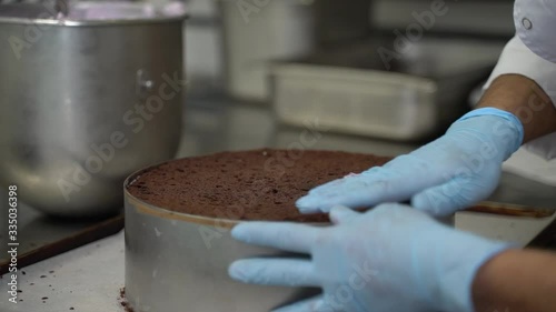Pastry chef in rubber gloves is cutting chocolate sponge cake on slices with big knife. Hands close-up. photo