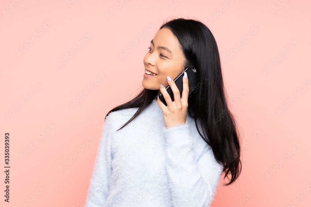 Teenager Chinese woman isolated on pink background keeping a conversation with the mobile phone with someone Teenager Chinese woman isolated on pink background keeping a conversation with the mobile phone with someone