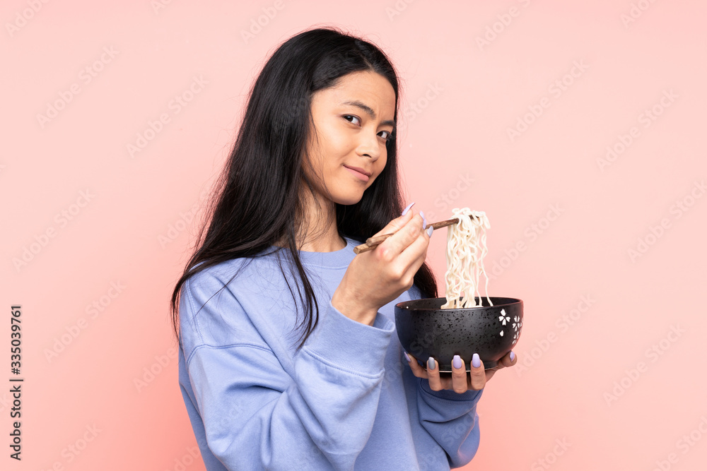 Teenager Asian woman isolated on beige background holding a bowl of noodles with chopsticks Teenager Asian woman isolated on beige background holding a bowl of noodles with chopsticks