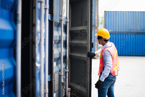Young Asian man worker foreman open the door of shipping Containers at commercial shipping dock felling serious. Engineer inspection. Cargo freight ship import export concept.
