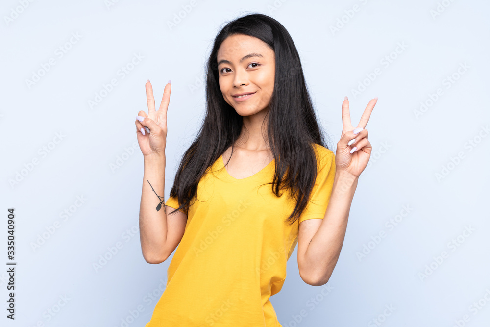 Teenager Chinese woman isolated on blue background showing victory sign with both hands Teenager Chinese woman isolated on blue background showing victory sign with both hands