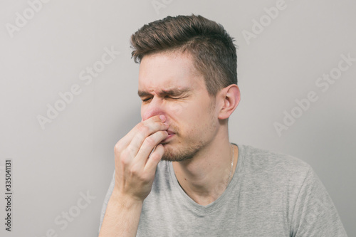 Young man sneezes in hand on gray background