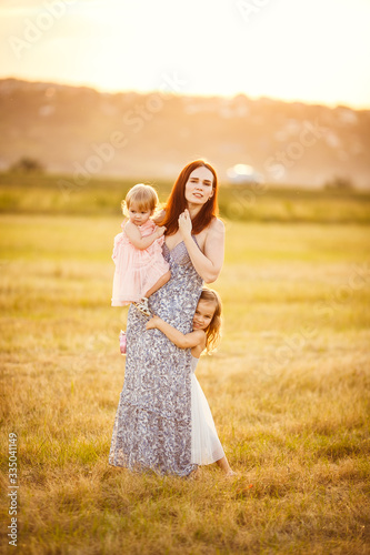 mom with daughters stand and hug on mowed field