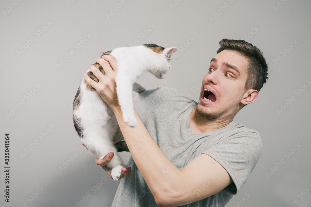 Young man with cute funny cat on light background Young man with cute funny cat on light background