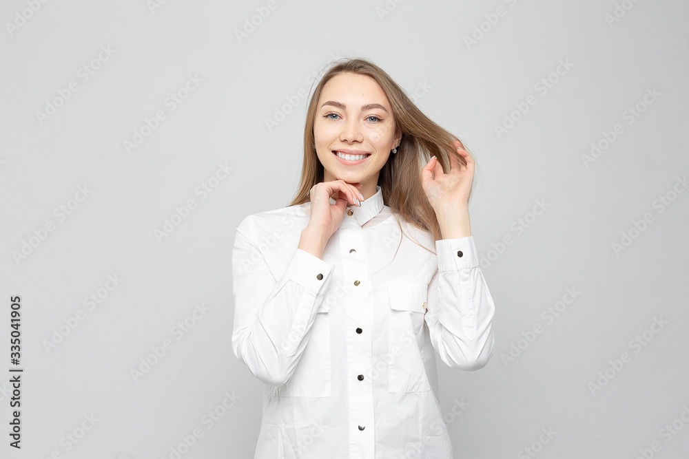 Beautiful young woman portrait. Portrait of a beautiful smiling blonde in white shirt on a white-gray. woman straightens her hair or holds her head Beautiful young woman portrait. Portrait of a beautiful smiling blonde in white shirt on a white-gray. woman straightens her hair or holds her head