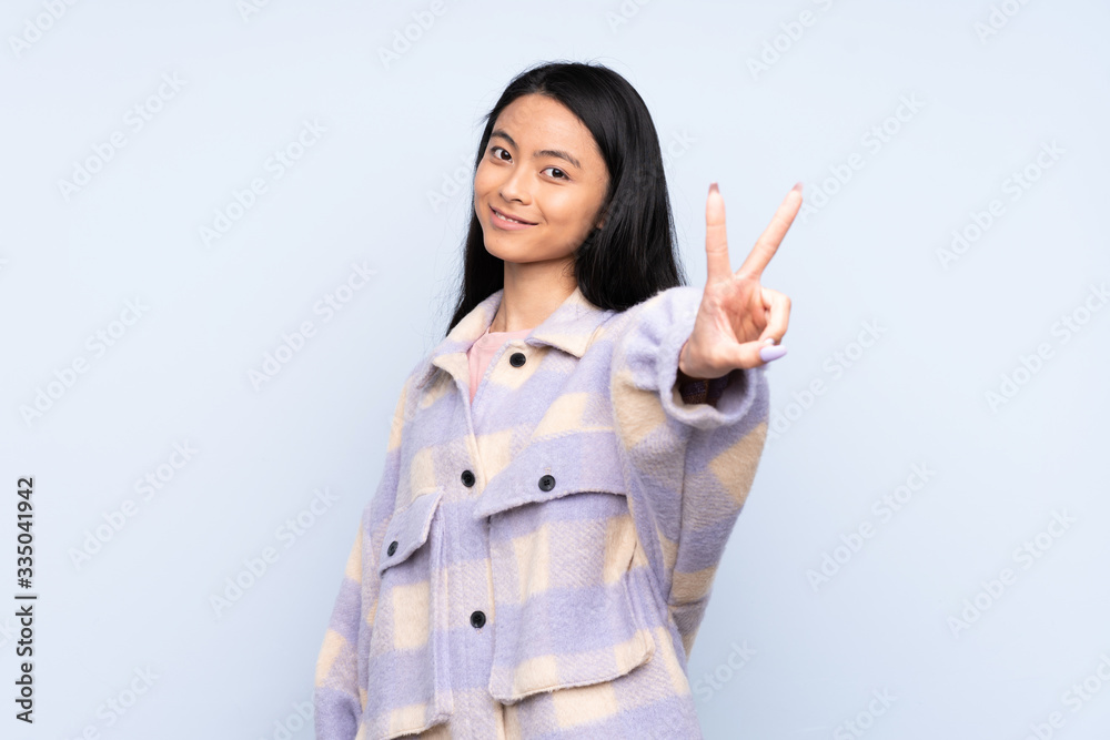 Teenager Chinese woman isolated on blue background smiling and showing victory sign Teenager Chinese woman isolated on blue background smiling and showing victory sign
