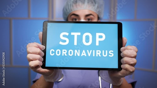 Caucasian female woman doctor nurse in a scrub cap, protective medical face mask, a stethoscope, and medical gloves, using a tablet computer device to say STOP CORONAVIRUS during the COVID-19 worldwid photo