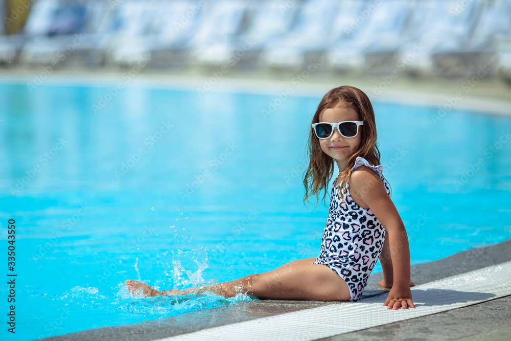 Great stay! child A girl sits near the hotel pool in the summer in sunglasses.