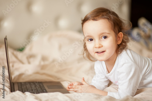 Little cute girl lying on the bed and using a digital tablet laptop notebook.