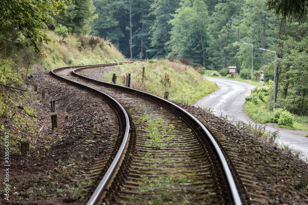 Railway curve and asphalt winding road in a green forest. Two communication and transport routes lying next to each other Railway curve and asphalt winding road in a green forest. Two communication and transport routes lying next to each other