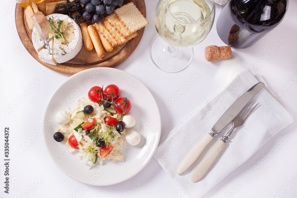 vegetables salad on the plate, glass of white wine and plate with assorted cheese, fruit and other snacks. vegetables salad on the plate, glass of white wine and plate with assorted cheese, fruit and other snacks.