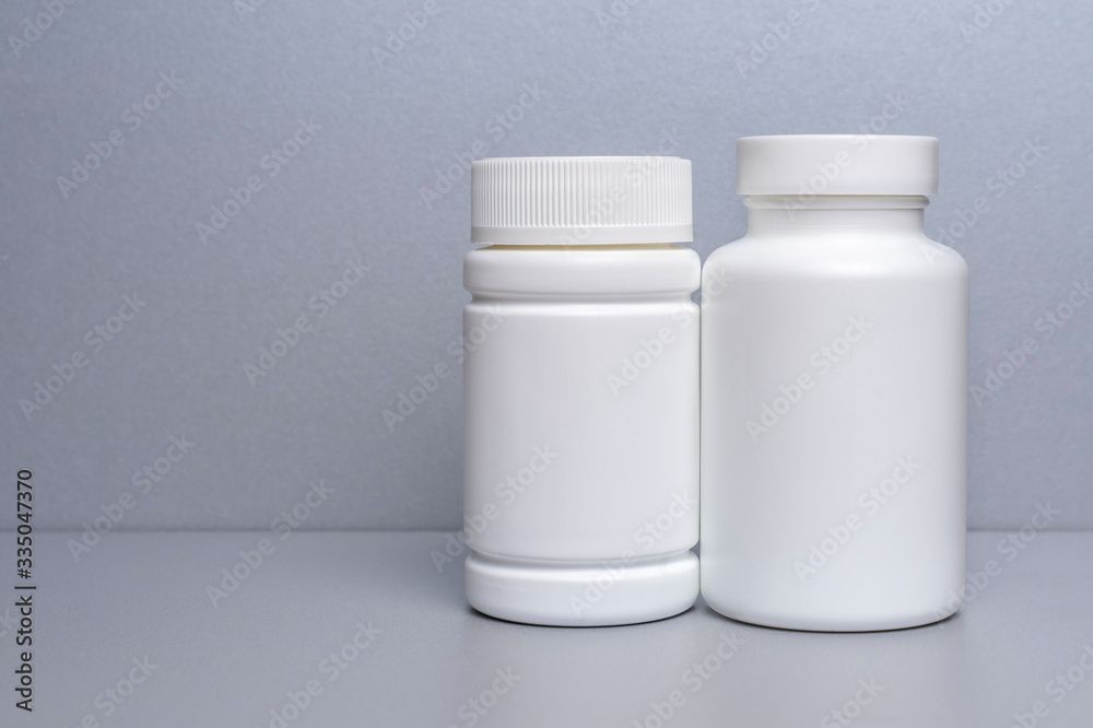 2 white jars for medicines and vitamins and dietary supplements without a name are on a gray shelf. copy space to the left. layout for a pharmacy, a store