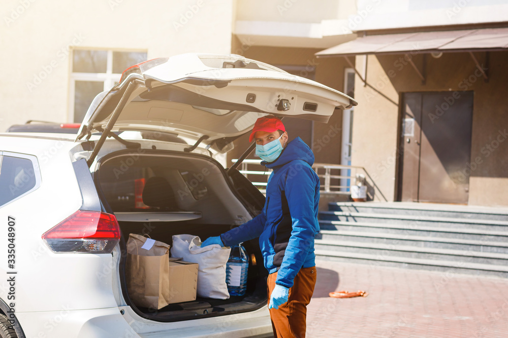 Delivery man holding paper bag with food near the car, food delivery man in protective mask Delivery man holding paper bag with food near the car, food delivery man in protective mask