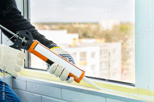 Bild auf Leinwand Contractor hand holding glue gun with silicone to repair tile and window