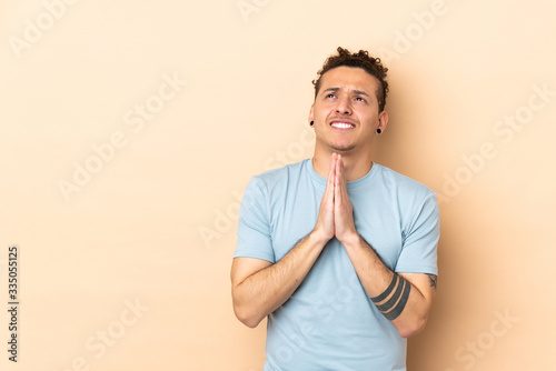 Caucasian man over isolated background keeps palm together. Person asks for something