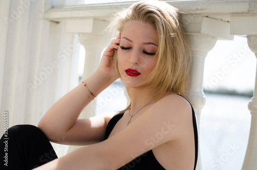 Young beautiful girl. Blonde posing while sitting by the column. Red lipstick on the lips. Photo of a model in nature.