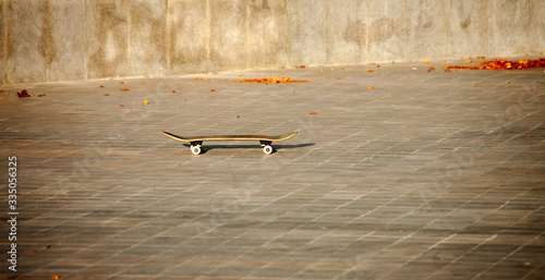 A skateboard stands alone on a stone block in a skatepark in the autumn sunset sunlight