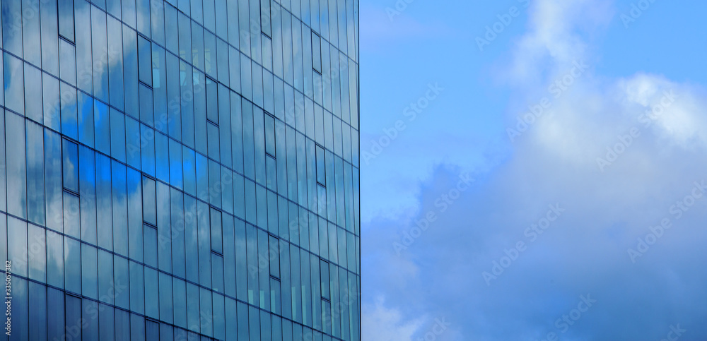 Fragment of the facade of a glass building against the sky with reflection of clouds