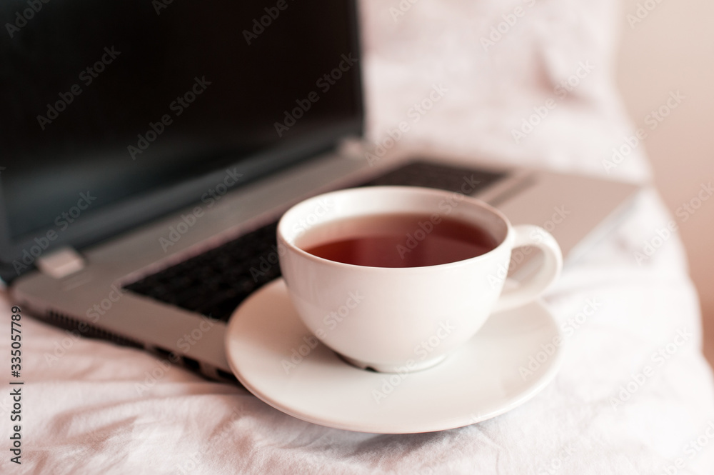 Cup of black tea on computer in bed closeup. Good morning. Breakfast time. Social distancing. Stay at home. Cup of black tea on computer in bed closeup. Good morning. Breakfast time. Social distancing. Stay at home.